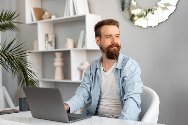 Hombre barbudo elegante que trabaja en la computadora portátil desde casa sentado en la mesa