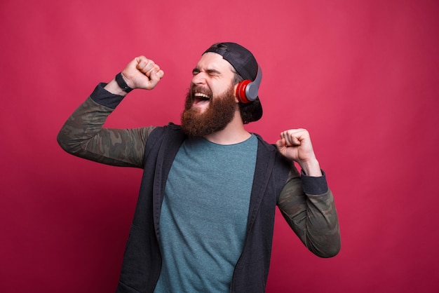 Hombre barbudo emocionado está cantando mientras escucha la música a través de auriculares