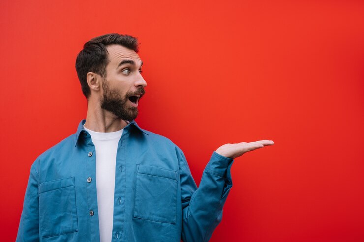 Foto hombre barbudo emocional apuntando con la mano, aislado sobre fondo rojo. copie el espacio, concepto de publicidad