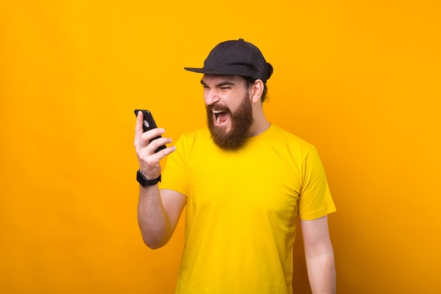 Hombre barbudo enojado gritando en el teléfono inteligente mientras habla con alguien