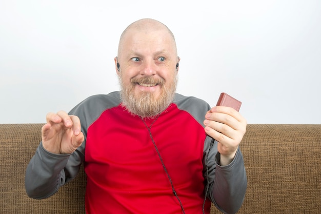 Hombre barbudo escucha con placer en casa su música favorita desde el teléfono con pequeños auriculares. audiófilo y amante de la música. música y sonido de alta fidelidad.