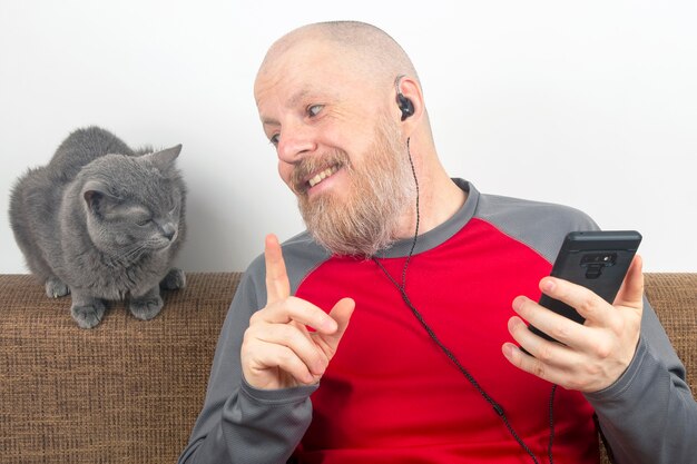 Hombre barbudo escucha con placer en casa su música favorita desde el teléfono con pequeños auriculares.