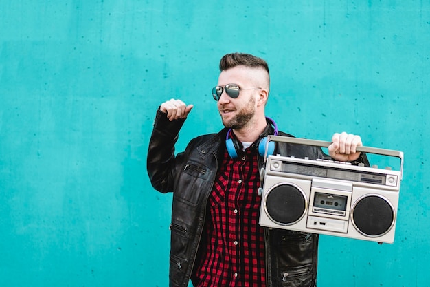 Foto hombre barbudo escuchando música con un estéreo boombox vintage y bailando al aire libre contra una pared azul un hombre genial divirtiéndose bailando en la calle con un reproductor de cintas vintage