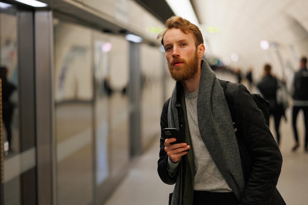 El hombre barbudo está parado en la plataforma de una estación de metro