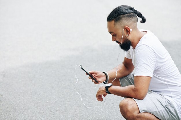 Hombre barbudo con estilo que controla la aplicación en el teléfono inteligente cuando pasa tiempo al aire libre