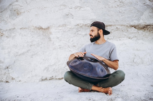 Hombre barbudo con estilo sosteniendo un instrumento musical hecho a mano único tocando en la cima de una montaña