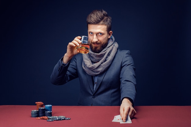 Hombre barbudo con estilo en traje y bufanda jugando en casino oscuro