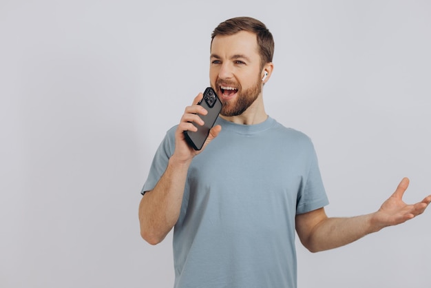 Hombre barbudo feliz bailando con auriculares escuchando música en auriculares con teléfono móvil y sonriendo complacido de pie sobre fondo blanco.