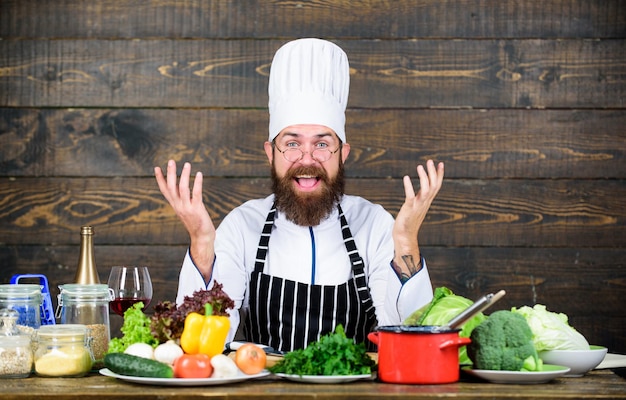 Hombre barbudo feliz cocinando en la cocina Dieta con alimentos orgánicos Verduras frescas Vitamin man use utensilios de cocina Chef profesional en uniforme de cocinero Comida saludable y vegetariana Alimentación saludable para usted
