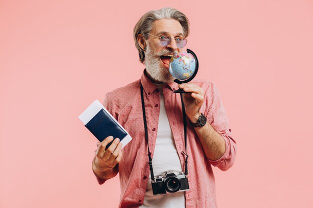 Hombre barbudo feliz en gafas de sol con una cámara y pasaporte elige un país en globo para viajar.