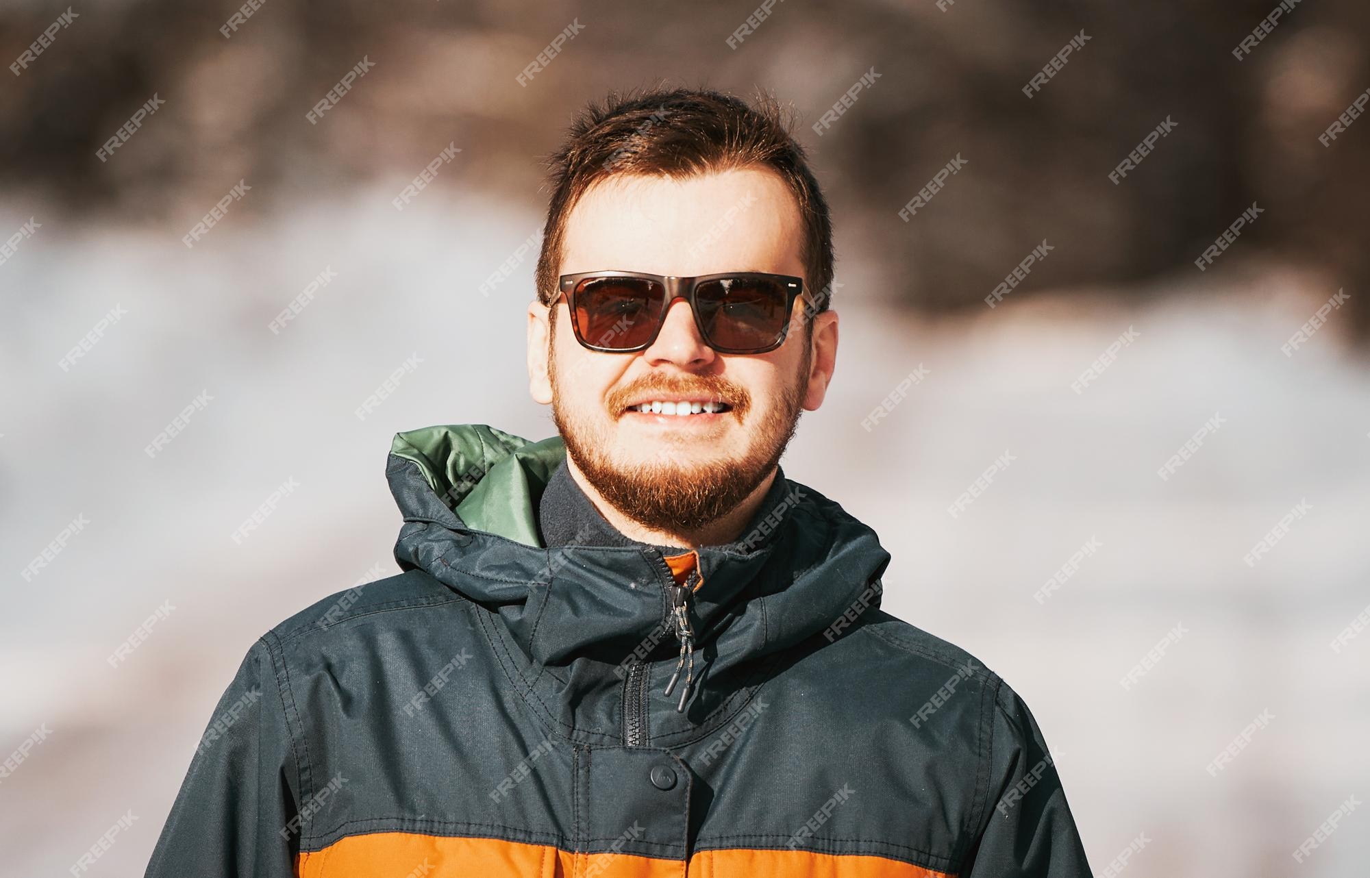 Hombre barbudo feliz con gafas de sol en un clima soleado y nevado concepto  de pasar tiempo activo caminando después de una ventisca de nieve el tipo  sonriendo y usando una chaqueta de invierno