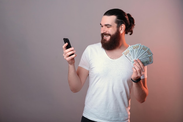 El hombre barbudo feliz tiene un montón de dinero y su teléfono