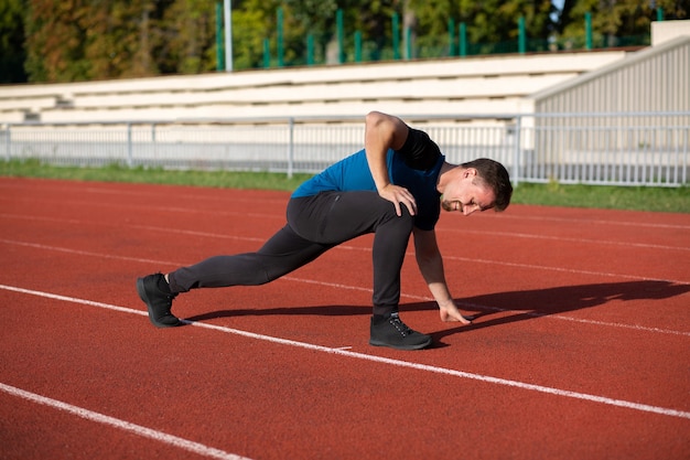 Foto hombre barbudo fuerte que hace estiramientos después de correr en el staduim. espacio vacio