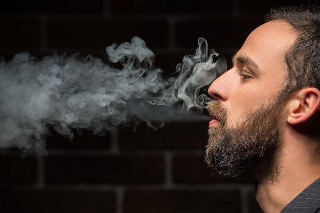 Hombre barbudo fuma contra la pared de ladrillo.