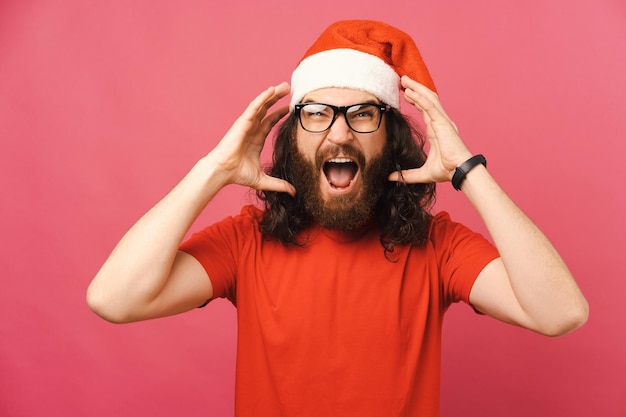 Hombre barbudo furioso con un sombrero de Navidad grita y gesticula sobre su cabeza