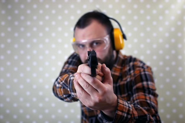 Hombre barbudo con gafas protectoras y entrenamiento auditivo en tiro con pistola