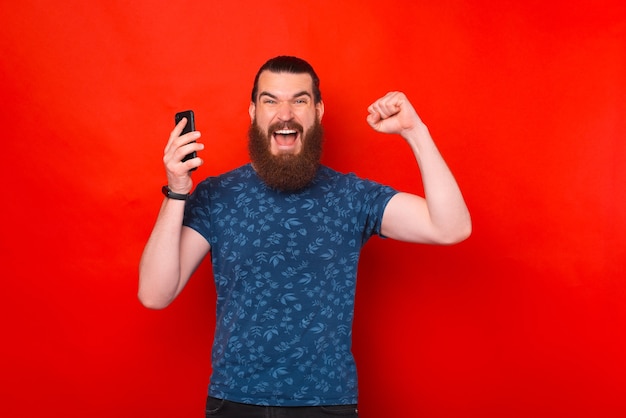 Un hombre barbudo ganador sostiene su teléfono y grita a la cámara.