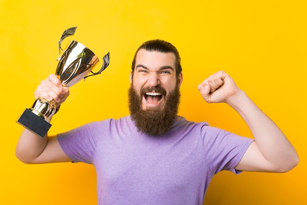 Foto hombre barbudo gritando está haciendo el gesto de ganador y sosteniendo un trofeo.