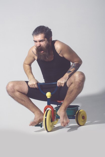 Hombre barbudo gritando sentado en bicicleta colorida juguete