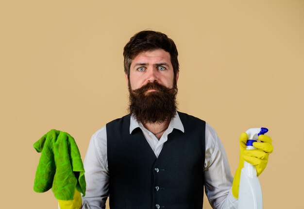 Hombre barbudo en guantes de goma uniformes con productos de limpieza hombre limpiador de servicio doméstico con trapo