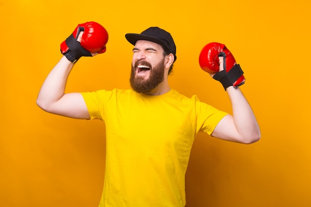 Hombre barbudo guapo alegre celebrando la victoria y con guantes de boxeo