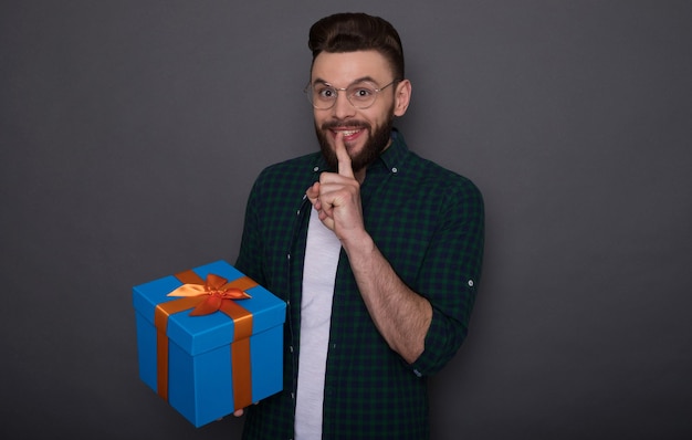 Hombre barbudo guapo emocionado en ropa casual de buen humor con una gran caja de regalo en sus manos muestra un gesto de sorpresa