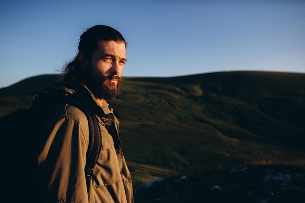 Foto hombre barbudo y guapo de pie junto a la montaña contra un cielo despejado