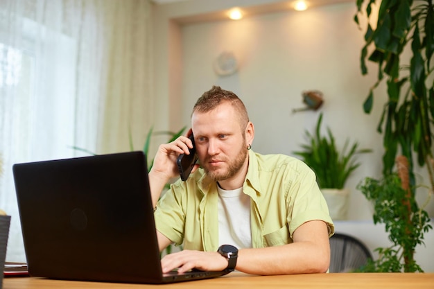 Hombre barbudo hablando por teléfono usando una computadora portátil