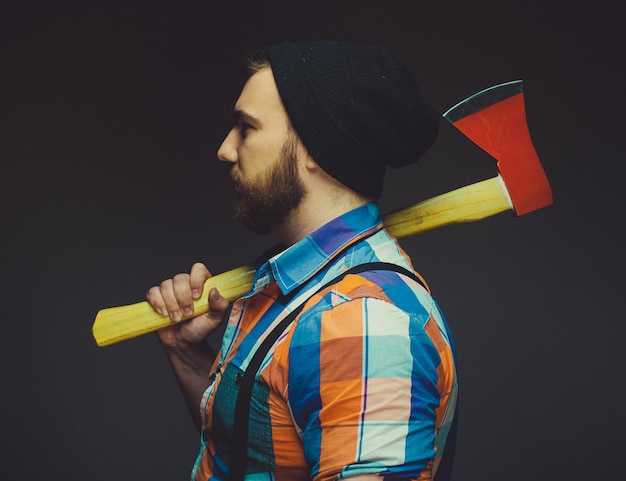 Foto hombre barbudo con hacha posando sobre fondo negro en estudio