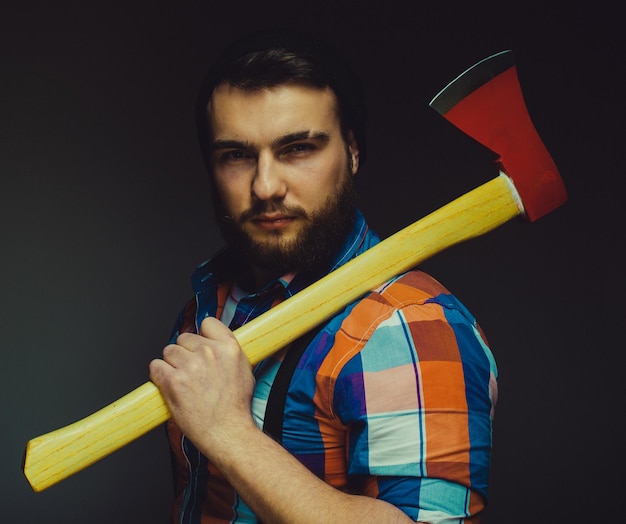 Hombre barbudo con hacha posando sobre fondo negro en estudio