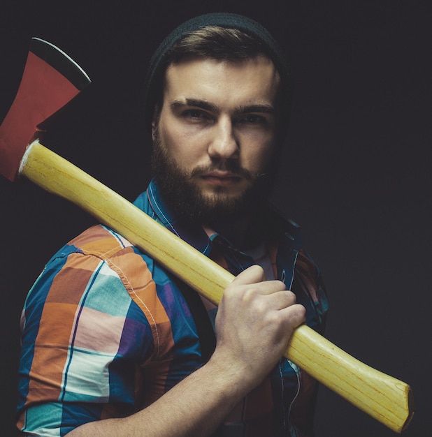 Hombre barbudo con hacha posando sobre fondo negro en estudio