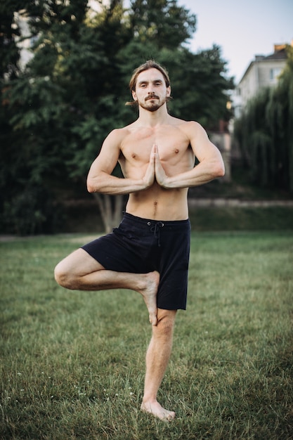 Hombre barbudo haciendo yoga en el parque verde