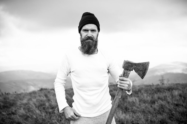 Hombre barbudo hipster con soporte de hacha en paisaje de montaña
