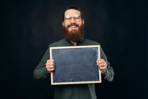 Foto un hombre barbudo inteligente sostiene una pizarra negra frente a su pecho foto de estudio sobre fondo negro