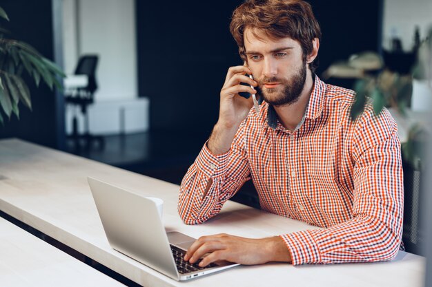 Hombre barbudo joven con camisa casual usando su computadora portátil. Retrato de hombre de negocios