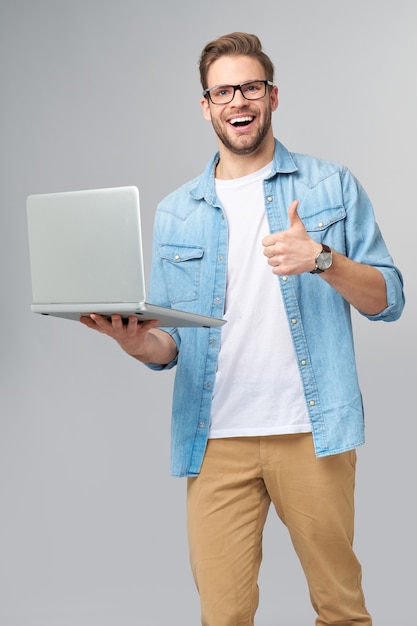 Hombre barbudo joven concentrado con gafas vestido con camisa de jeans sosteniendo portátil aislado