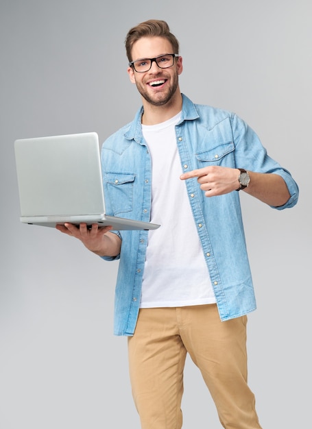 Hombre barbudo joven concentrado con gafas vestido con camisa de jeans sosteniendo portátil aislado