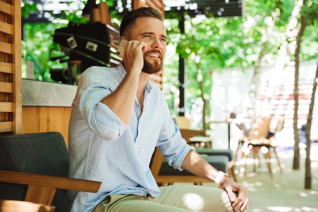 Hombre barbudo joven feliz hermoso que habla por teléfono móvil.