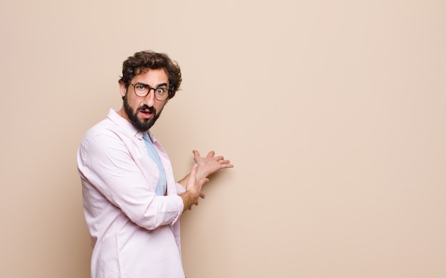 Hombre barbudo joven que expresa un concepto contra la pared plana