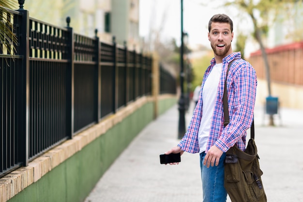 Hombre barbudo joven sorprendido en fondo urbano. Concepto de estilo de vida