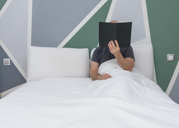 Foto hombre barbudo leyendo un libro en una cama blanca