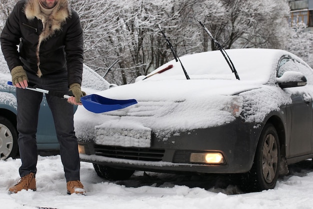Hombre barbudo limpia la nieve de un coche en una mañana de invierno