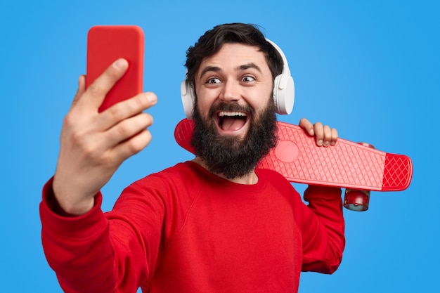 Hombre barbudo con longboard tomando selfie