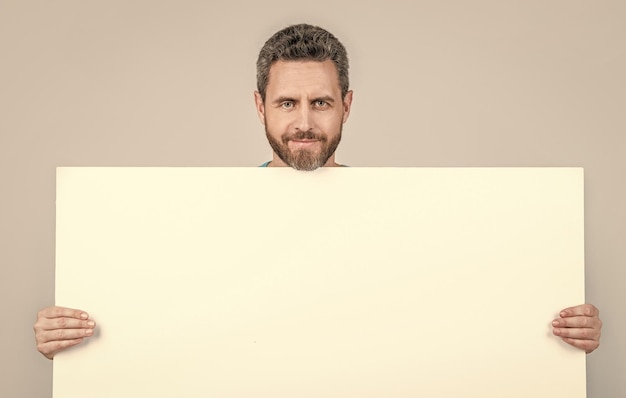 Hombre barbudo maduro sonriente detrás de una pancarta de papel blanco en blanco con espacio de copia para la presentación de la oferta