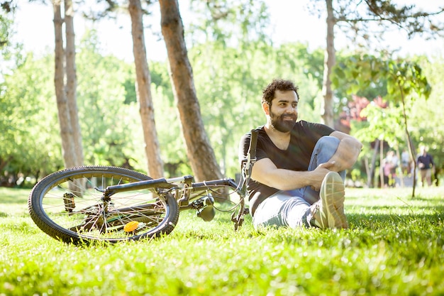 Hombre barbudo mirando a la cámara con su bicicleta junto a él en el parque. Deporte y salud