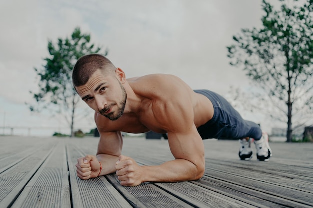 Foto el hombre barbudo motivacional se para en una pose de tablón entrena los músculos y tiene un cuerpo fuerte