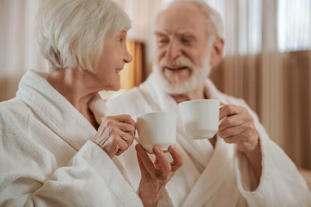 Un hombre barbudo y una mujer de cabello corto tomando café juntos y sonriendo el uno al otro