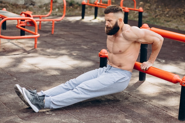 Hombre barbudo musculoso fuerte haciendo flexiones en barras asimétricas en el gimnasio de la calle al aire libre. Concepto de estilo de vida de entrenamiento.