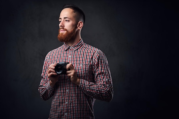 Hombre barbudo pelirrojo vestido con una camisa de lana roja tomando fotos con una cámara compacta.