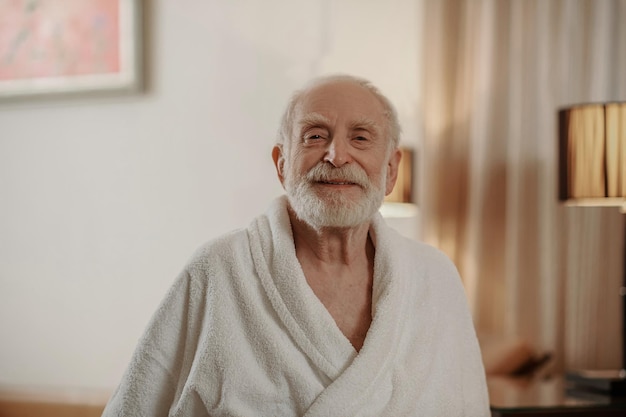 Un hombre barbudo de pelo gris con una túnica blanca en una habitación de hotel